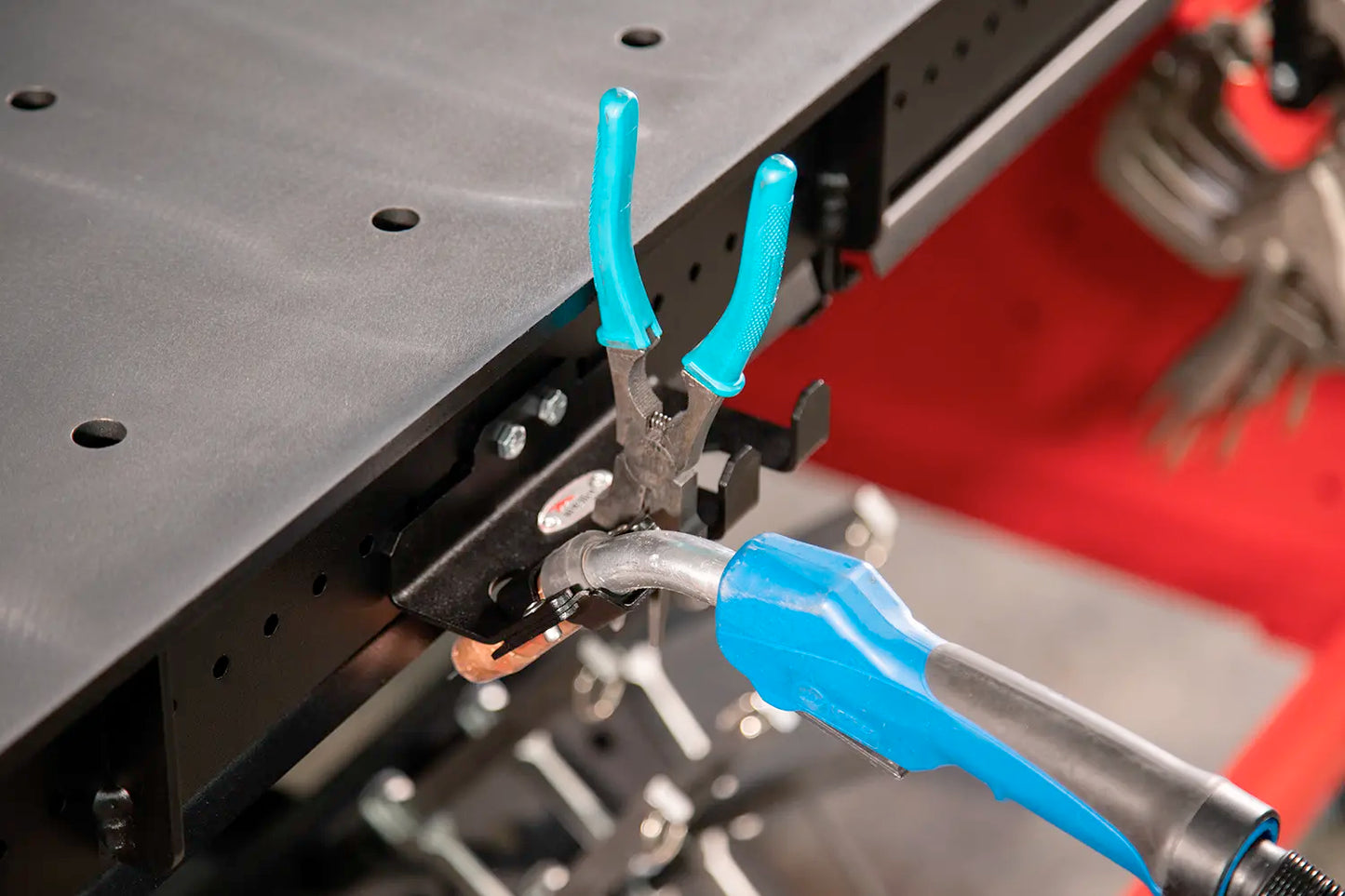 MIG torch and pliers stored along table edge